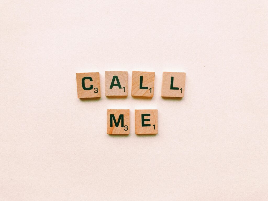 Contact Wooden letter tiles spelling 'Call Me' on a pastel pink background, invoking communication and connection.